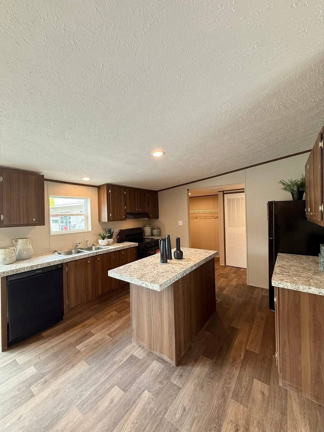 Spacious kitchen with wood cabinets, island, and marble countertops. Brightly lit by recessed lighting, featuring a cozy, modern design with plants.