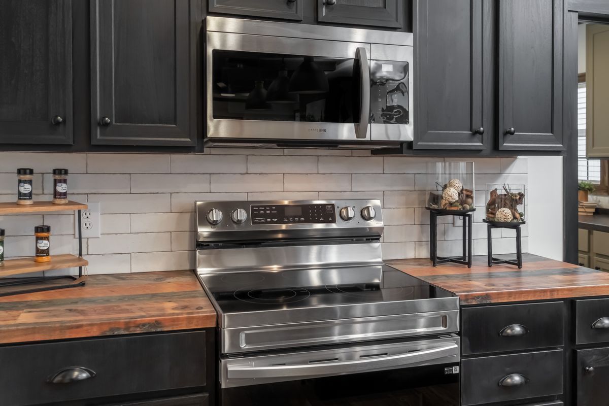 Modern kitchen with dark wood cabinets and stainless steel appliances, including a stove and microwave. Wooden countertops add warmth. Neutral color palette creates a sleek, inviting atmosphere.