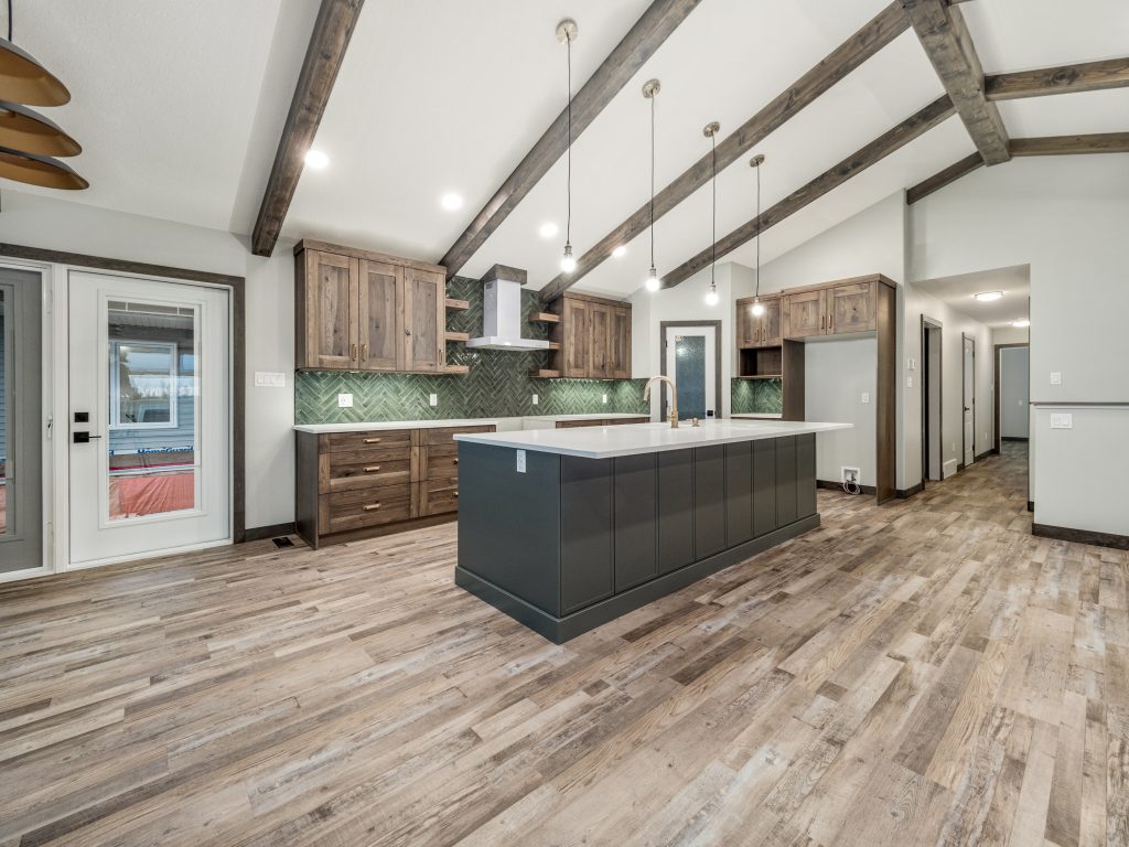 Spacious kitchen with rustic wood beams, modern dark island, and green herringbone backsplash. Warm tones and pendant lights create a cozy ambiance.