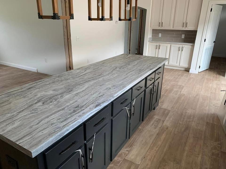 Modern kitchen with a large marble island featuring dark cabinets and sleek handles. Bright ambiance with wood flooring and neutral-colored cabinetry.