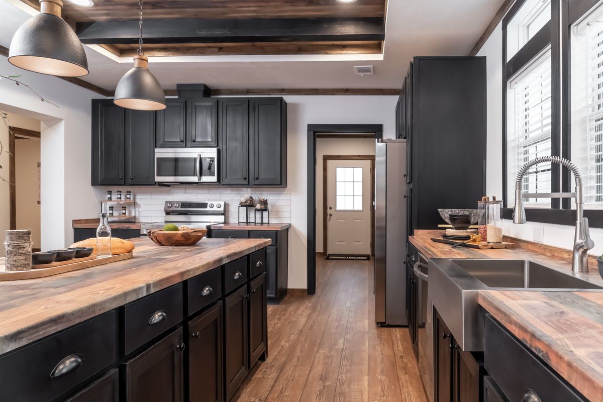 Modern kitchen with dark cabinets and wood countertops, featuring a farmhouse sink, stainless steel appliances, pendant lighting, and a warm, inviting ambiance.