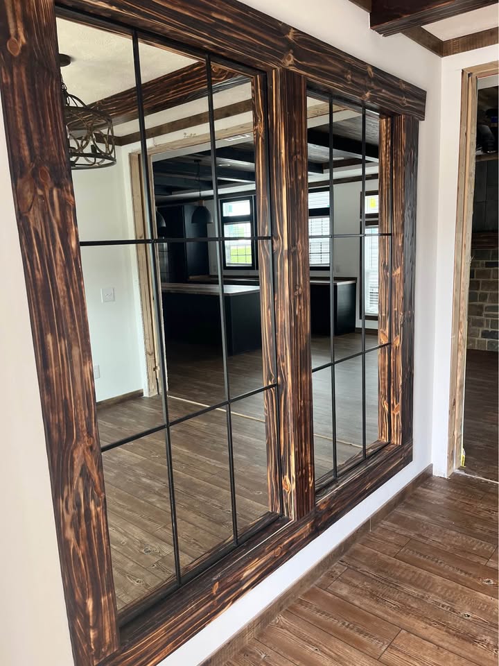 Rustic wooden mirrors with grid patterns reflect a cozy room with dark furniture and wooden floors. Soft lighting enhances a warm, inviting atmosphere.
