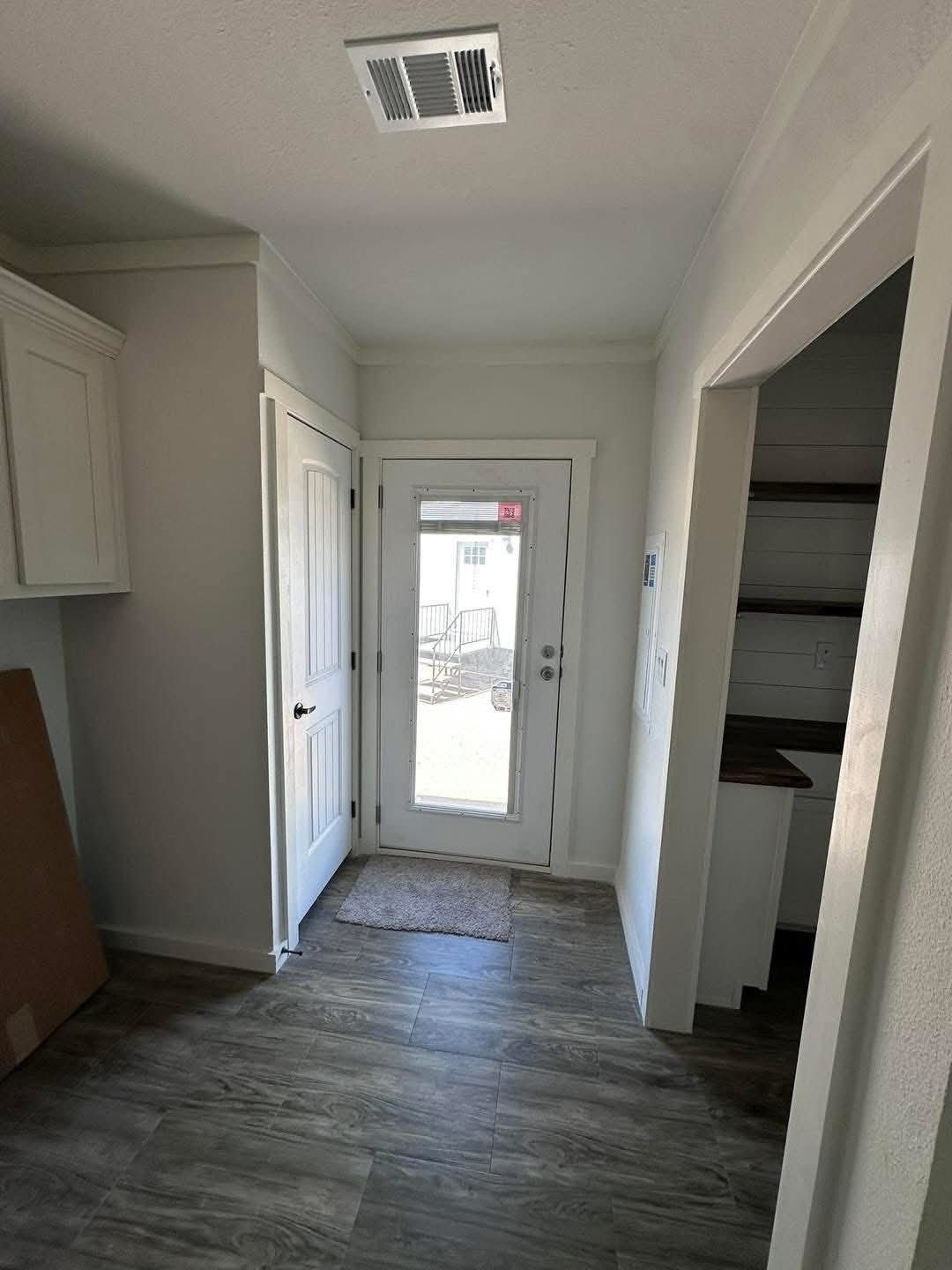 A simple room featuring a door on one side and a window on the opposite wall, with neutral-colored walls.