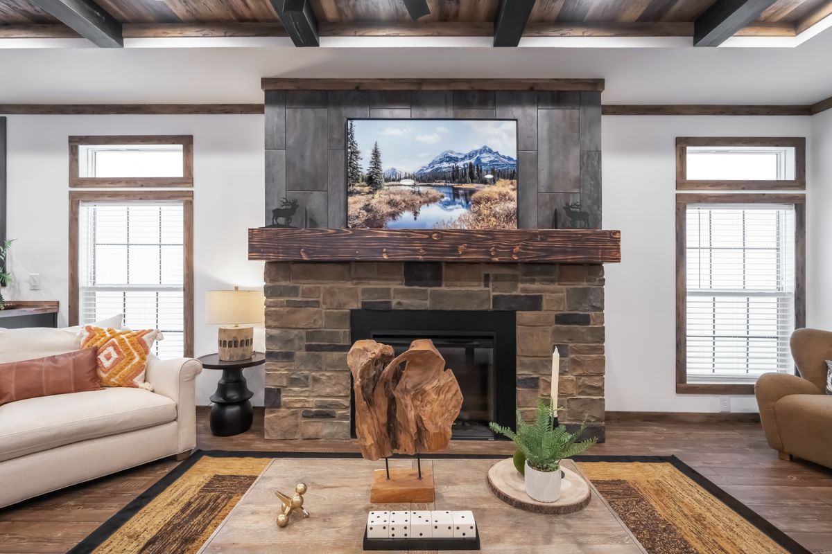 Living room with stone fireplace, modern art, a nature landscape on TV, and cozy seating. Decor includes wooden sculpture and leafy plant. Warm, inviting atmosphere.