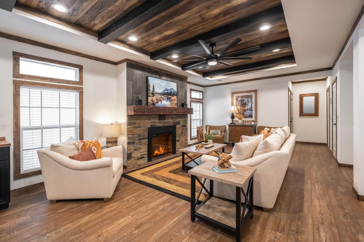 Cozy living room with wooden accents, featuring a stone fireplace and beige sofas. Warm lighting and decor create an inviting, rustic ambiance.