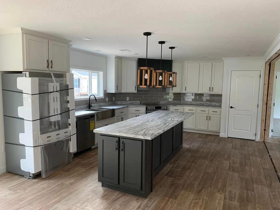 Modern kitchen with gray cabinets, marbled island, and wooden accents. New appliances await installation. Bright, clean, and inviting space.
