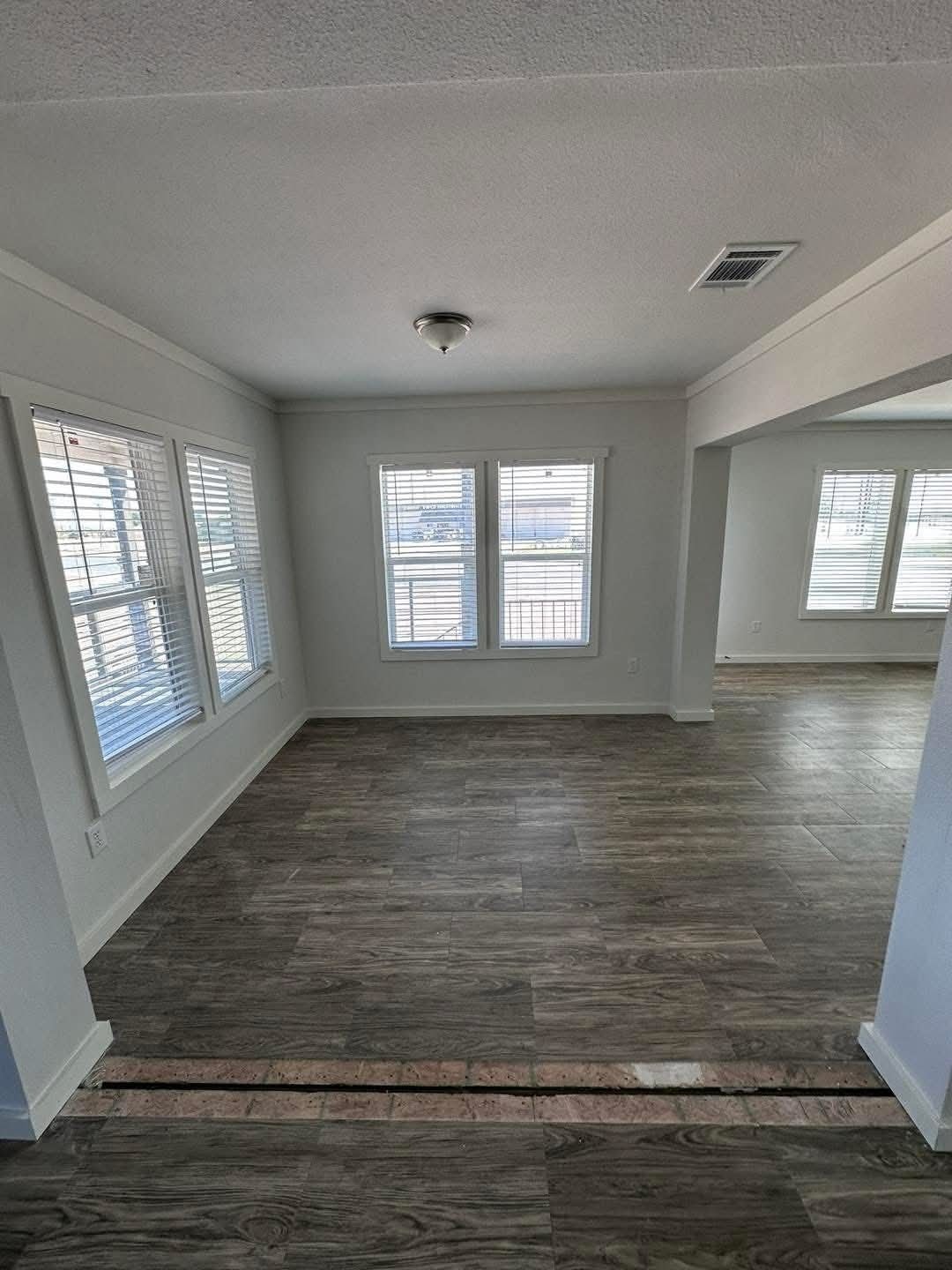 Empty living room featuring hardwood floors and large windows allowing natural light to fill the space.