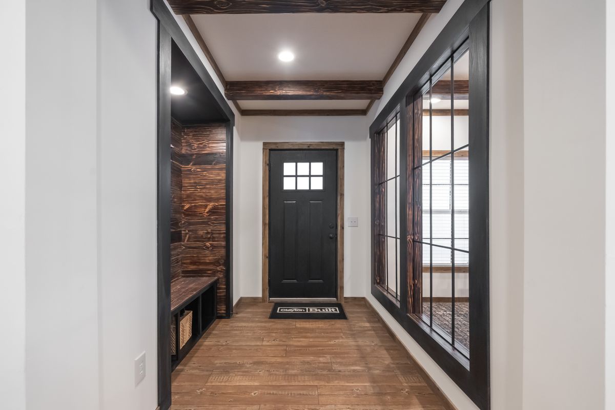 Modern hallway with a black front door, flanked by large windows. There's a cozy wooden bench with storage on the left and warm wood accents throughout.