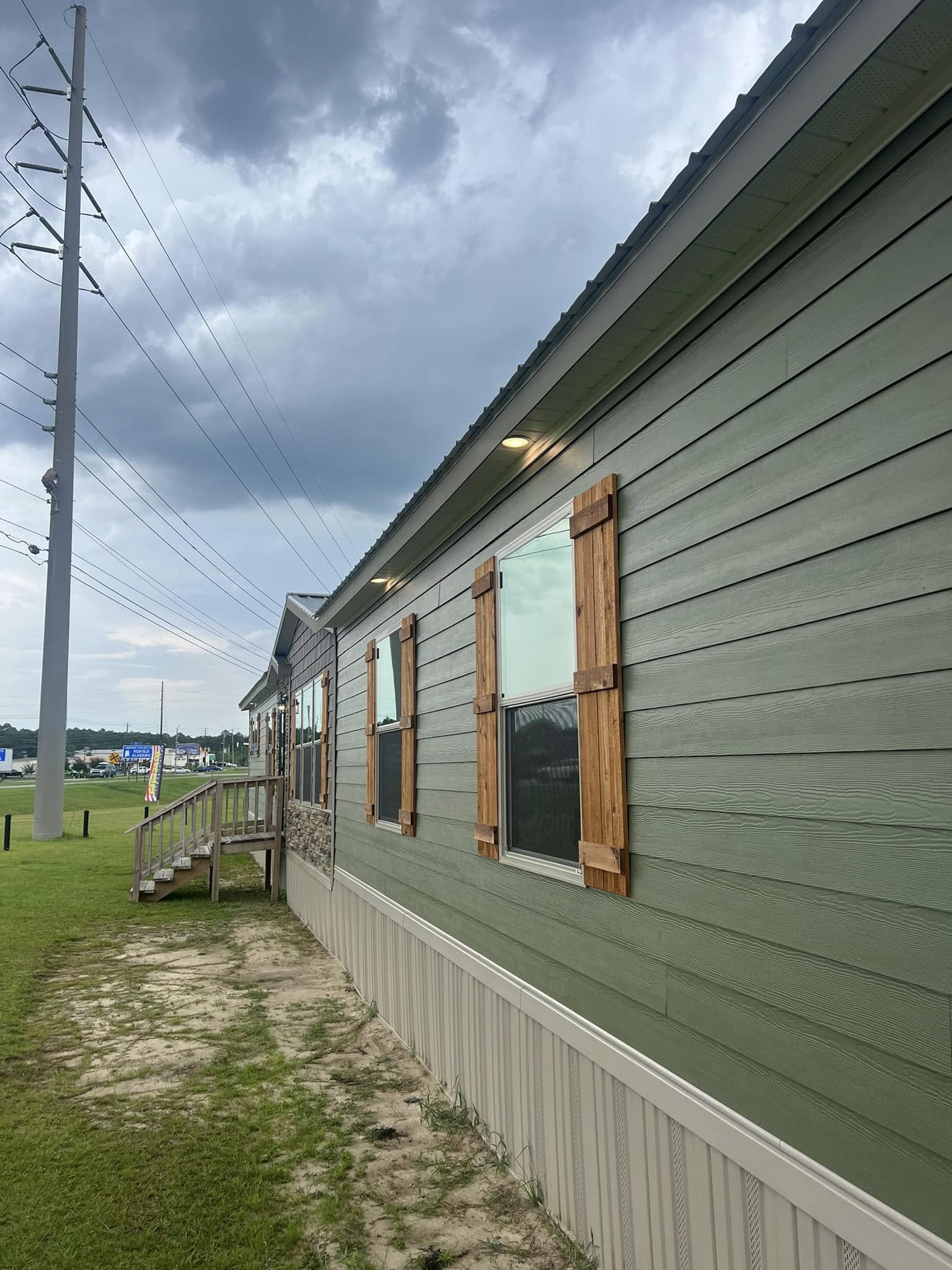 Side view of a green house with wooden window shutters and a stone-accented facade. Dark storm clouds loom overhead, creating a tense and moody atmosphere.