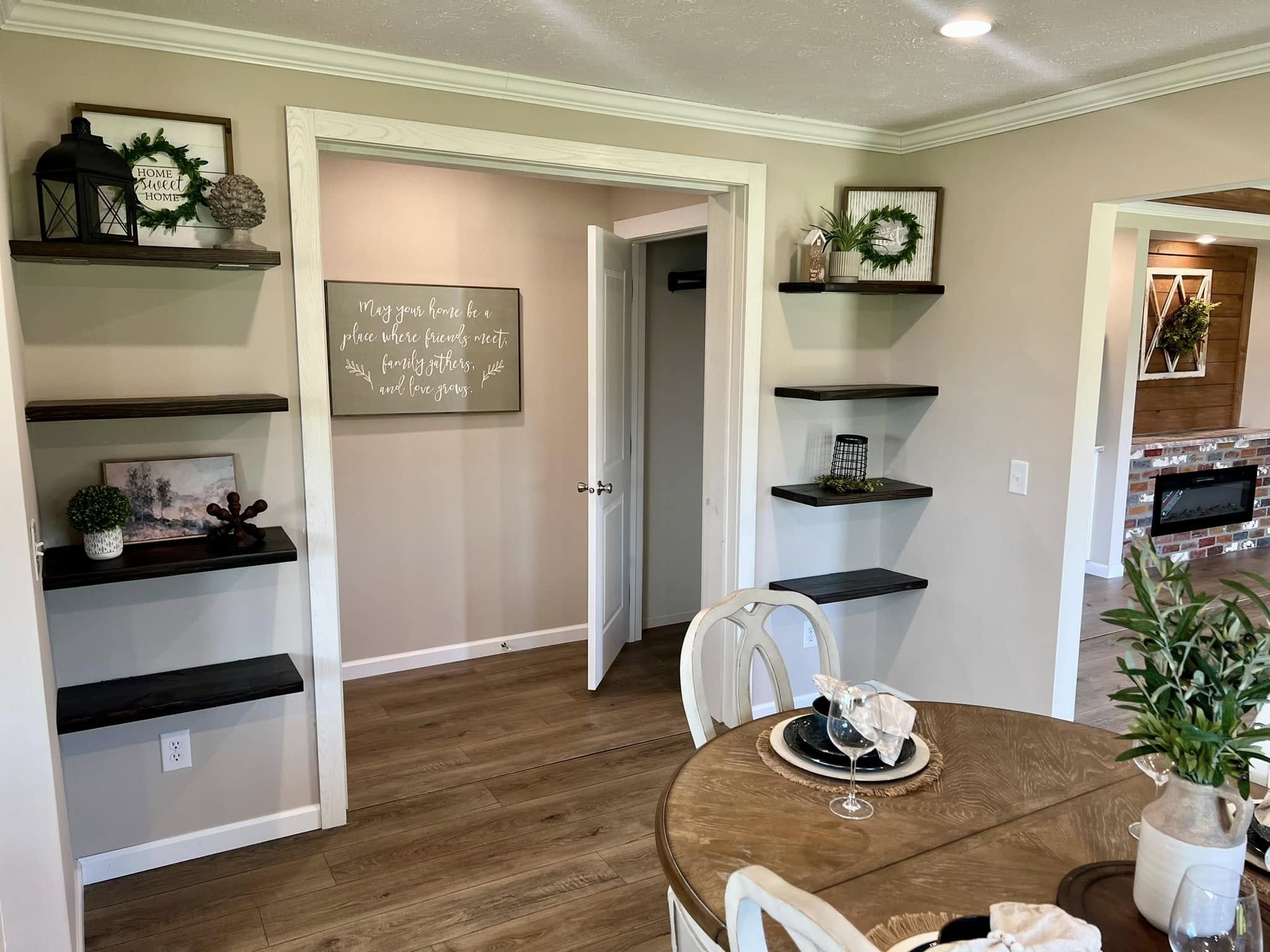 Cozy dining area with wooden table set for two, surrounded by shelves with decor. An inviting, homey atmosphere with neutral tones and soft lighting.