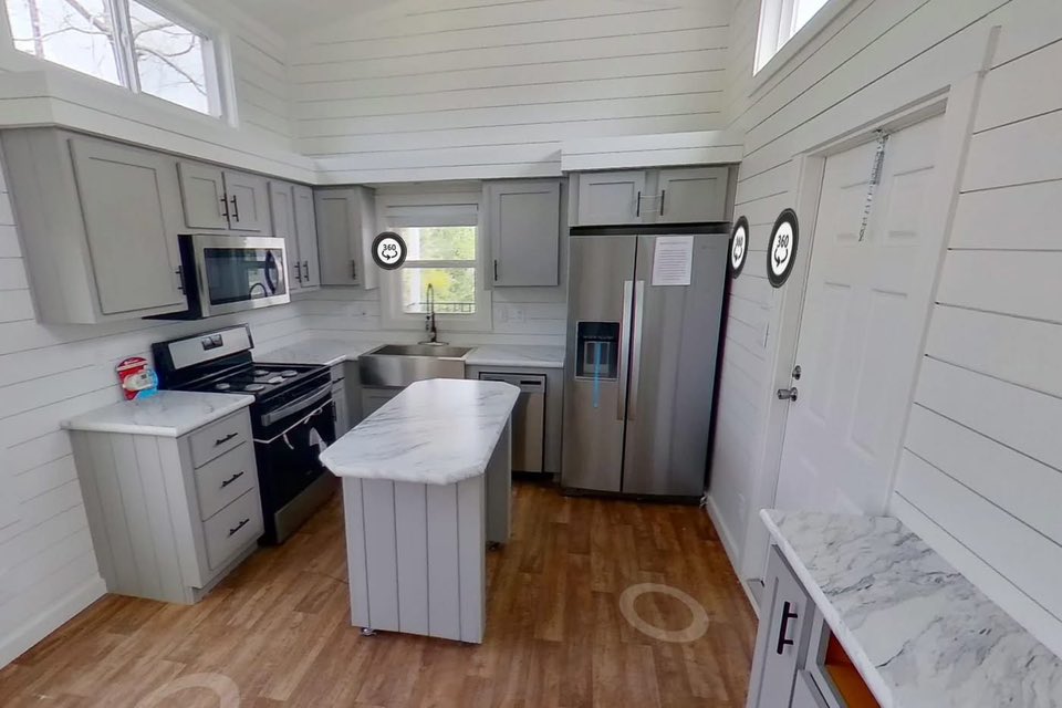 Modern kitchen with gray cabinets, stainless steel appliances, and marble countertops. Bright space with wood floors and high white shiplap walls.