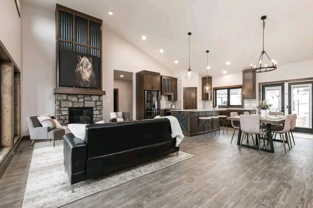 Spacious open-plan living room with high ceilings, featuring a stone fireplace, modern kitchen, and elegant dining area. Natural light and cozy atmosphere.