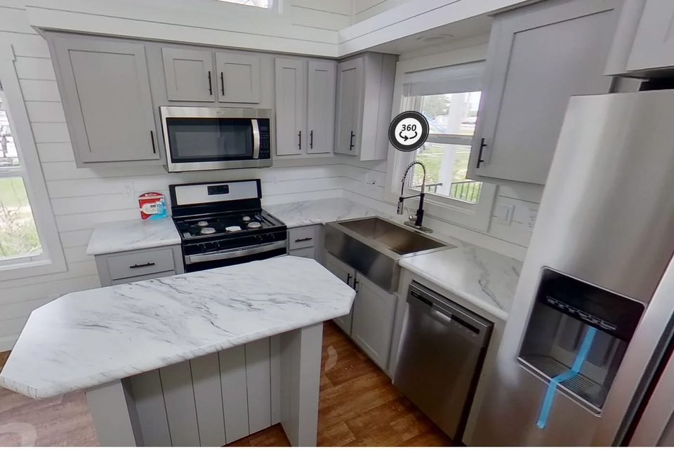 Compact, modern kitchen with gray cabinets, marble countertops, stainless steel appliances, and natural light from large windows. Cozy and inviting atmosphere.