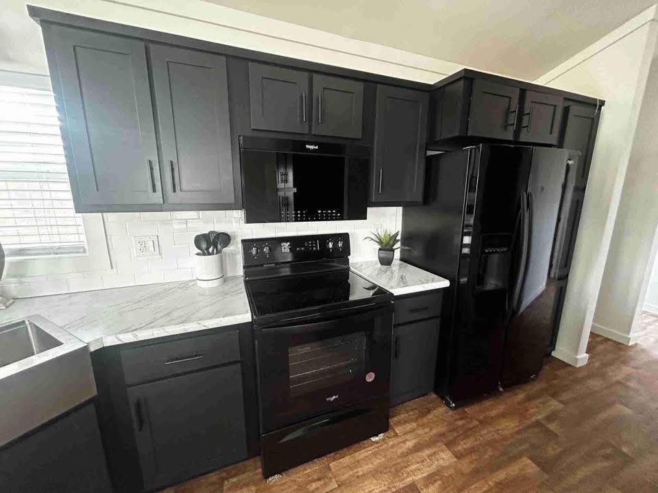 Modern kitchen with black cabinets and appliances, including a stove, microwave, and fridge. White marble countertops and subway tile backsplash add contrast.
