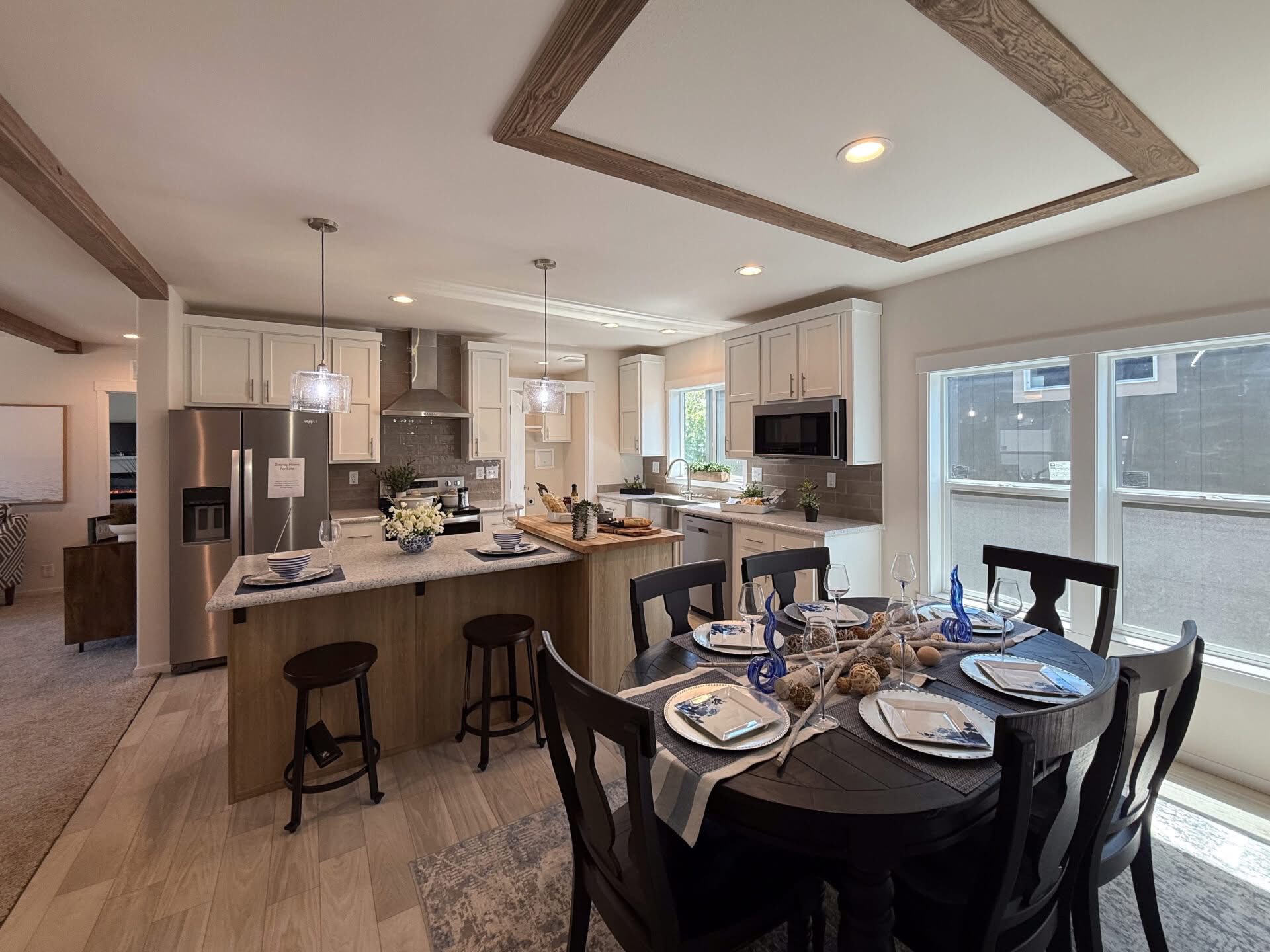 Modern kitchen and dining area with elegant decor. White cabinets, stainless steel appliances, and pendant lights over a wood island. Dining table set for six near large windows, creating a bright and welcoming atmosphere.