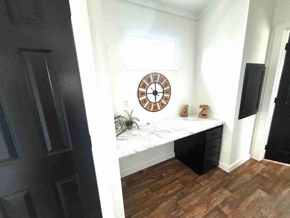 Marble desk in a small nook with a large clock on the wall, wooden floor, and black drawers. Minimalist décor with a calm, clean vibe.