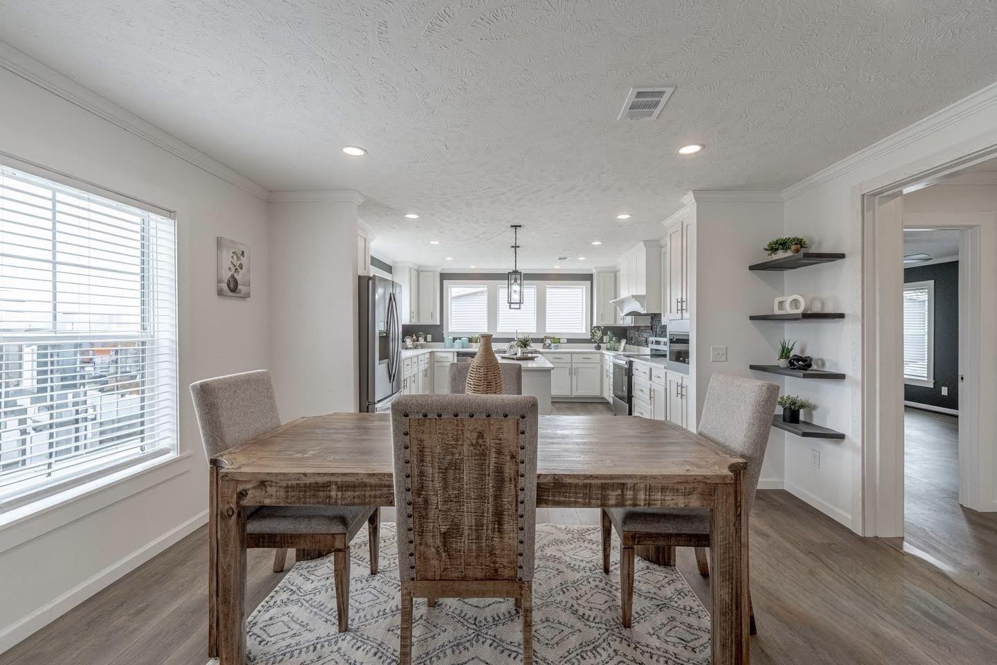 A spacious, modern kitchen and dining area with a wooden table and four chairs. Neutral tones, large windows, and sleek appliances create a cozy, inviting atmosphere.