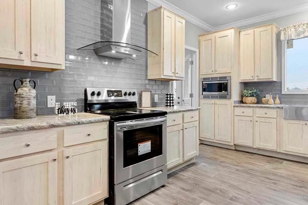 Spacious kitchen with light wood cabinets and gray subway tile backsplash. Features a stainless steel stove, modern range hood, and decorative accents.