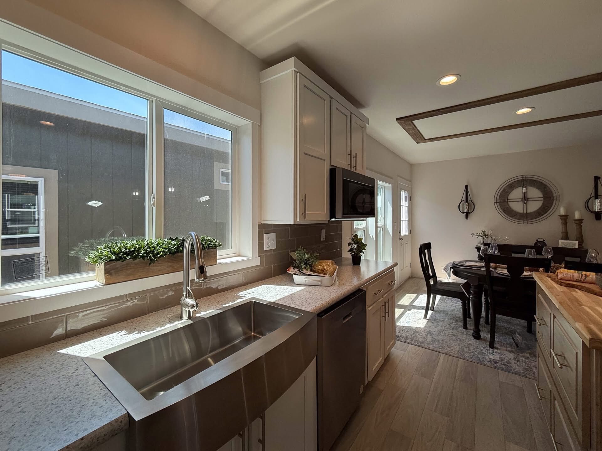 Bright kitchen with large window above a stainless steel sink, white cabinets, and a sleek countertop. Dining table set for four in the adjoining room.