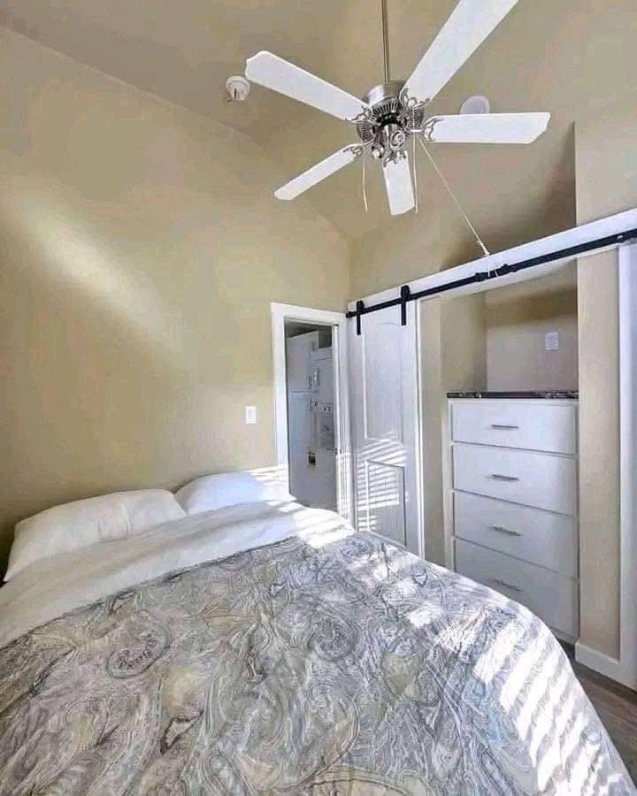 Cozy bedroom with a bed covered in a patterned duvet, next to white dressers under a sliding door. Sunlight filters through blinds, creating a warm atmosphere.