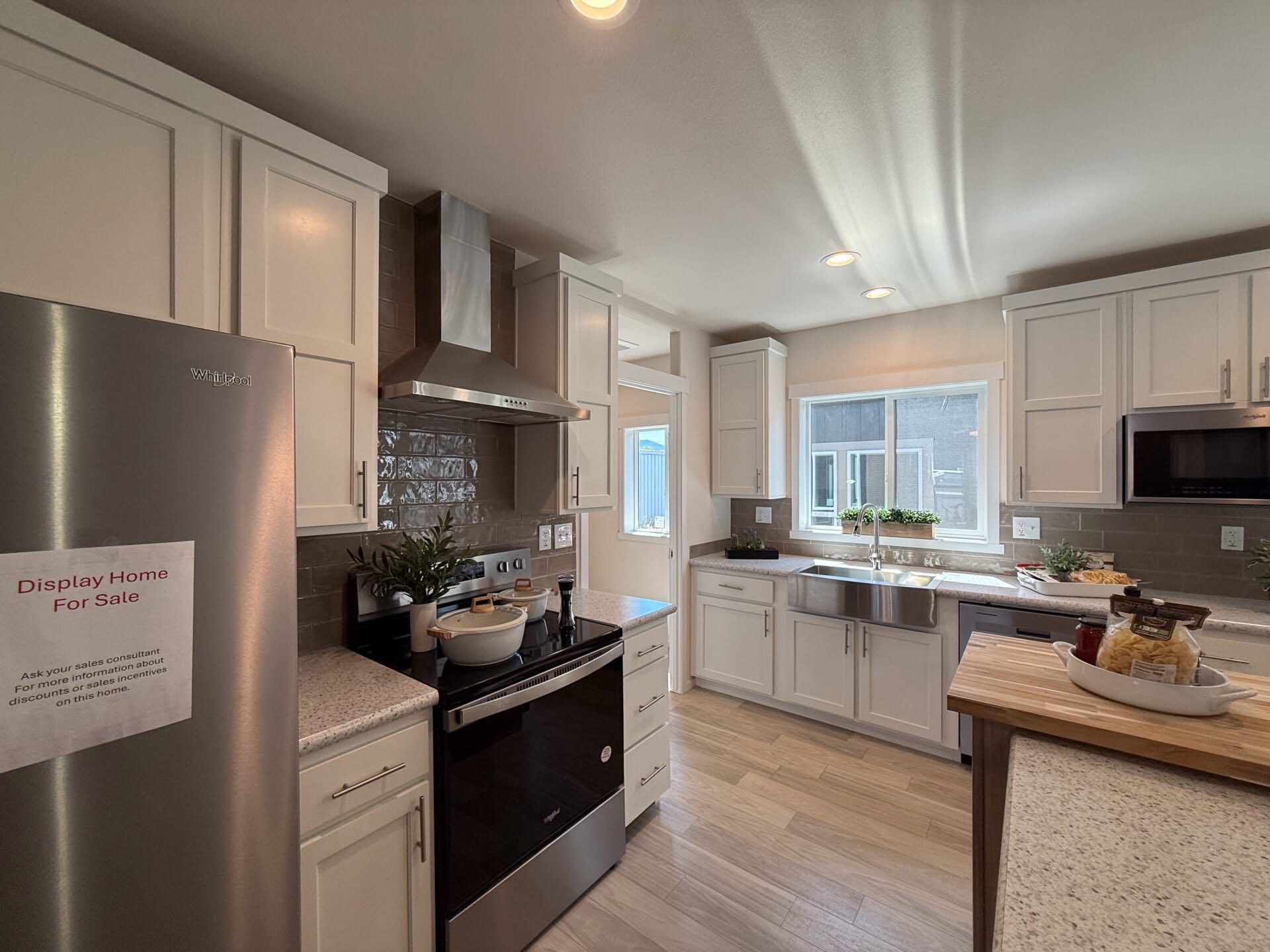 Modern kitchen with white cabinets, stainless steel appliances, and light wood flooring. Natural light fills the room through a window above the sink.