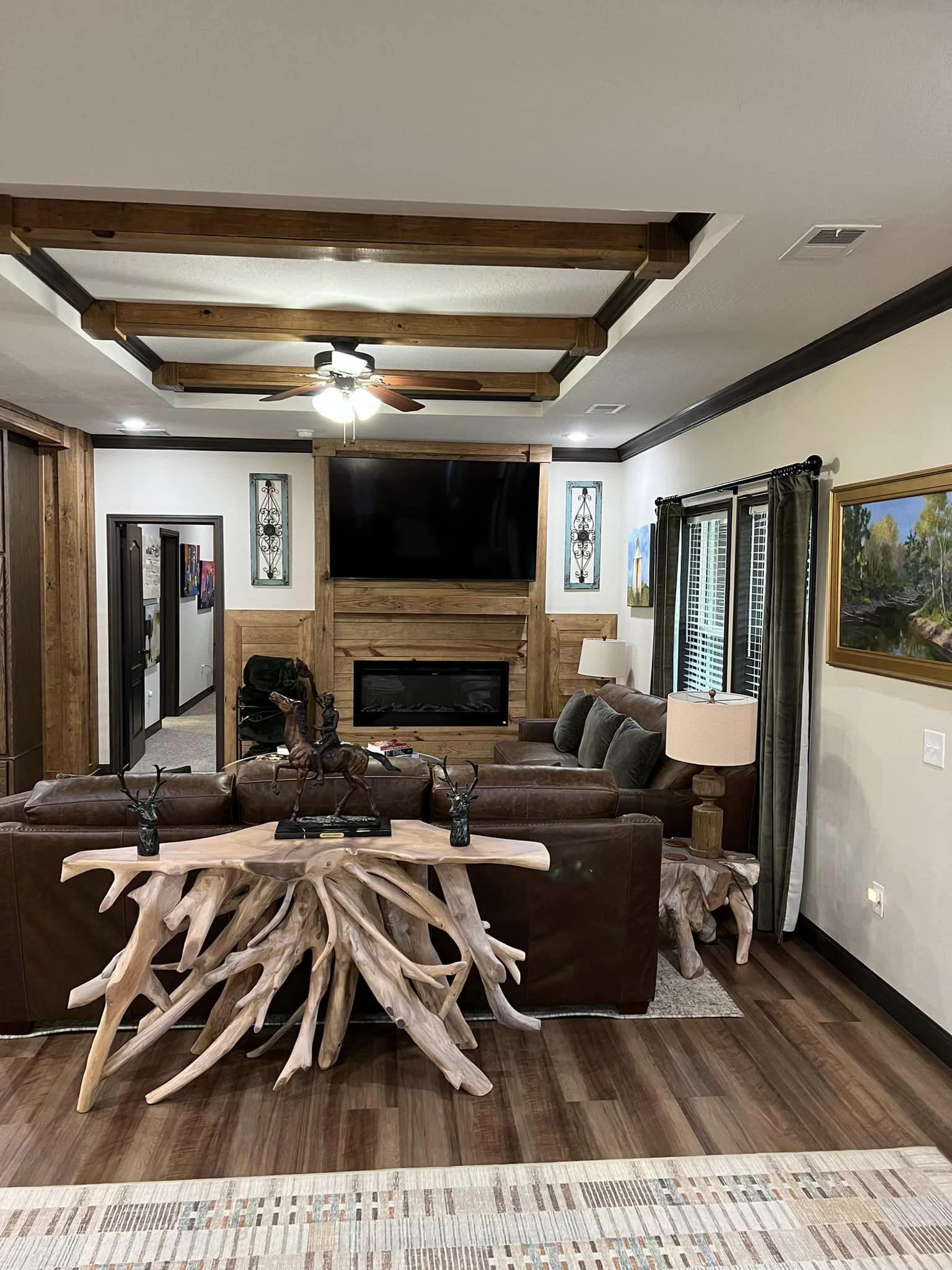 Cozy living room with a rustic vibe, featuring a brown leather sofa facing a wooden fireplace below a large TV. Unique driftwood table and modern decor.