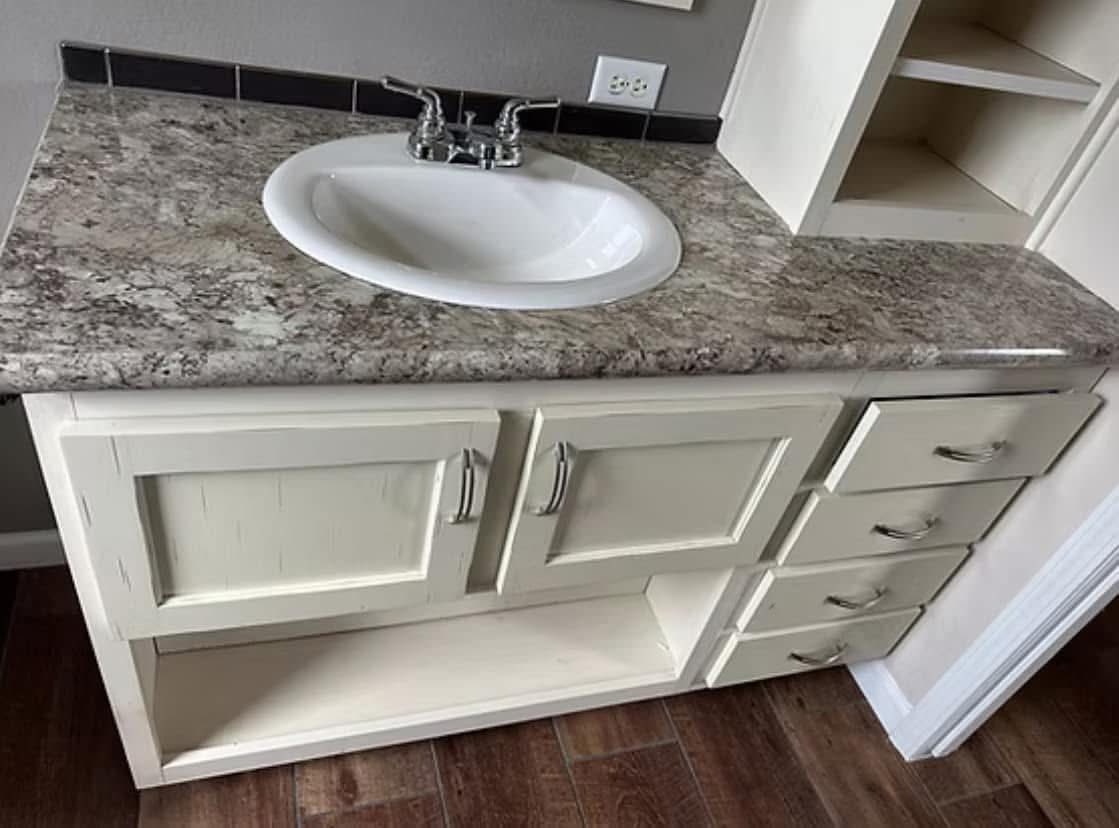 A bathroom vanity features a white sink set in a marble countertop with a beige cabinet. Four drawers are on the right, with two doors below the sink.