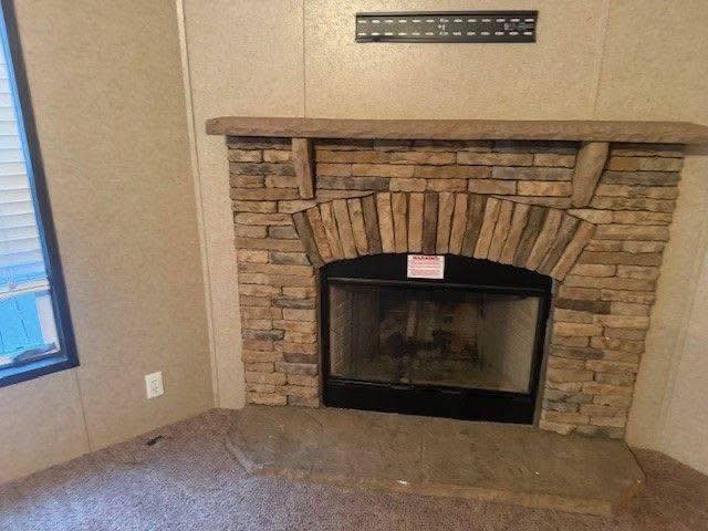 Stone fireplace in a cozy room with carpeted floor, brown wall tones, and a small window on the left. The atmosphere is warm and inviting.