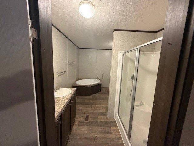 A modern bathroom with a wooden floor, featuring a glass shower on the right, a double sink with a granite countertop on the left, and a bathtub in the corner.