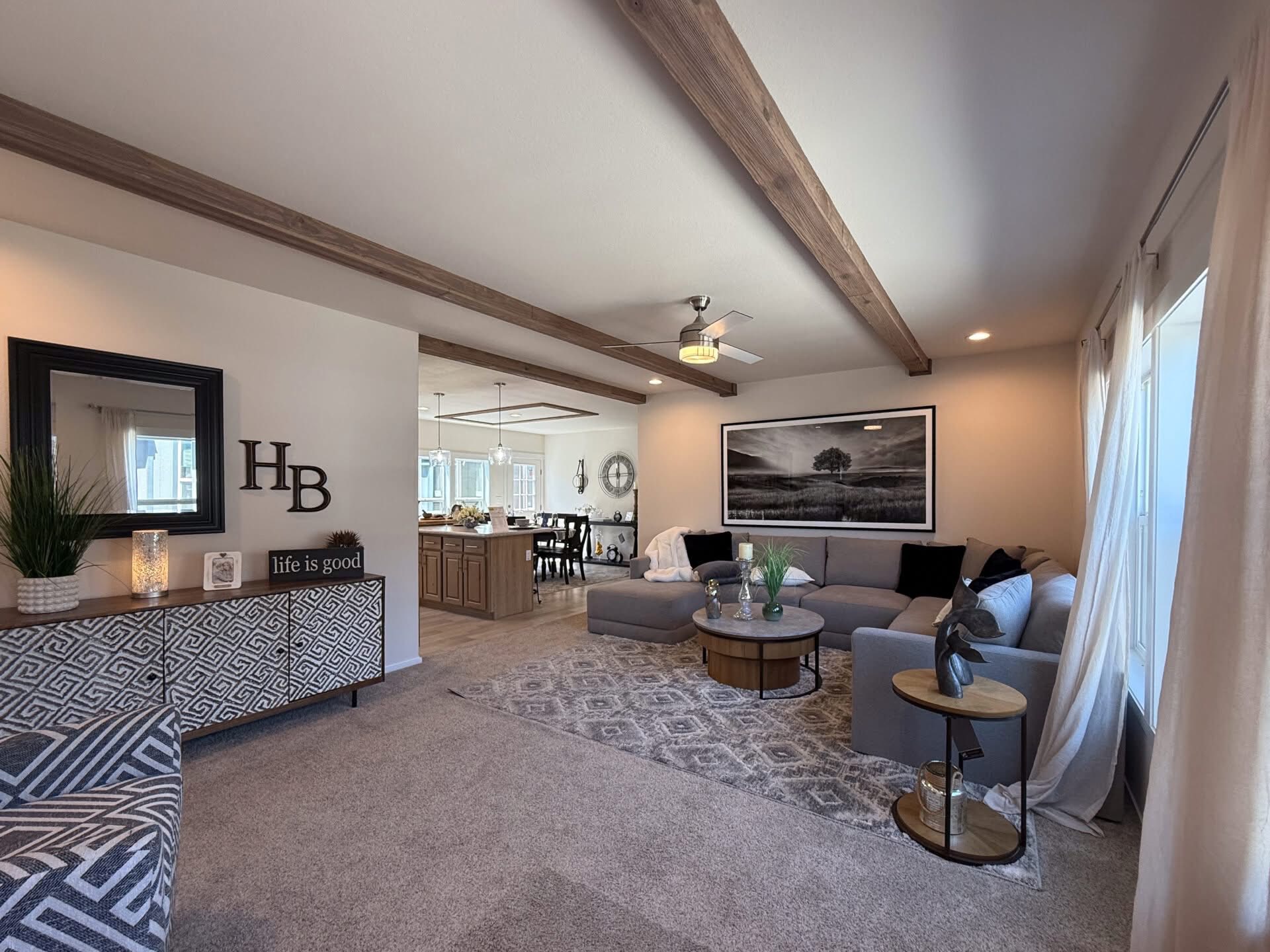 Spacious living room with wood beams, gray sectional sofa, and geometric rug. A sideboard with decor and large landscape photo add a cozy touch.