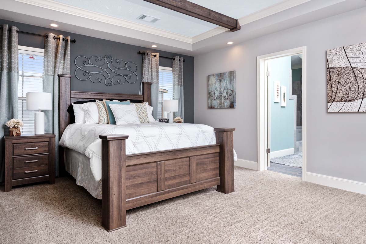 A cozy bedroom with a large wooden bed, white and teal bedding, two bedside tables, and curtains framing windows. Neutral tones and modern decor create a serene ambiance.