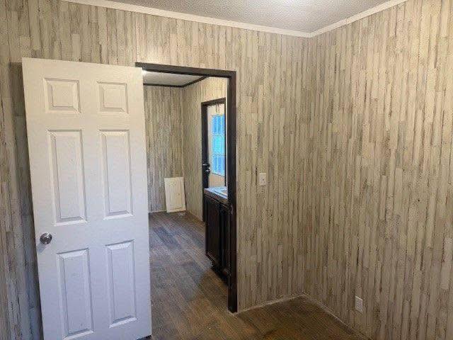 A room with wood-patterned wallpaper and wooden floors. An open white door reveals a sink and a small window in the adjacent room, creating a calm atmosphere.