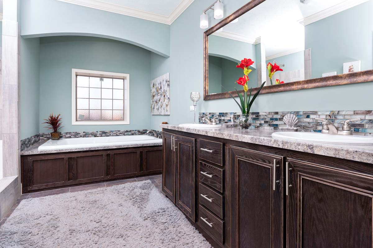 Spacious bathroom with a marble double sink vanity, large mirror, and a bathtub. Soft blue walls and vibrant red flowers create a calming ambiance.