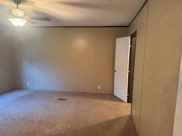 Empty beige room with carpeted floor, ceiling fan, and open white door. Soft lighting and simple decor create a neutral, calm atmosphere.