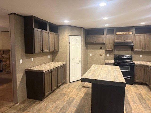 Modern kitchen with wood flooring, dark wood cabinets, and an island. Black appliances are featured, creating a cozy and contemporary atmosphere.