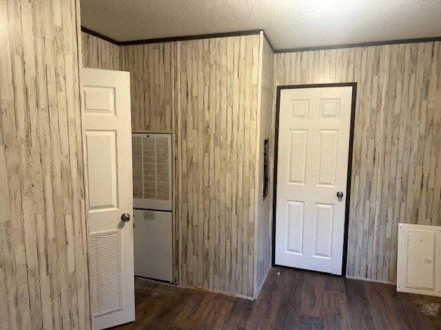 Room with wood-patterned wallpaper and two white doors, each with a knob. Dark wooden floor adds warmth. A utility panel is visible on one wall.