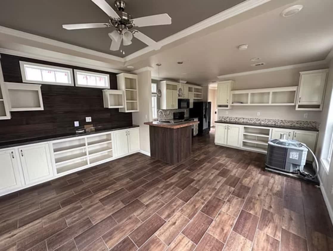 Spacious kitchen with dark wood floors, white cabinets, and ceiling fan. Central island, stainless steel appliances, and bright ambiance convey modern elegance.