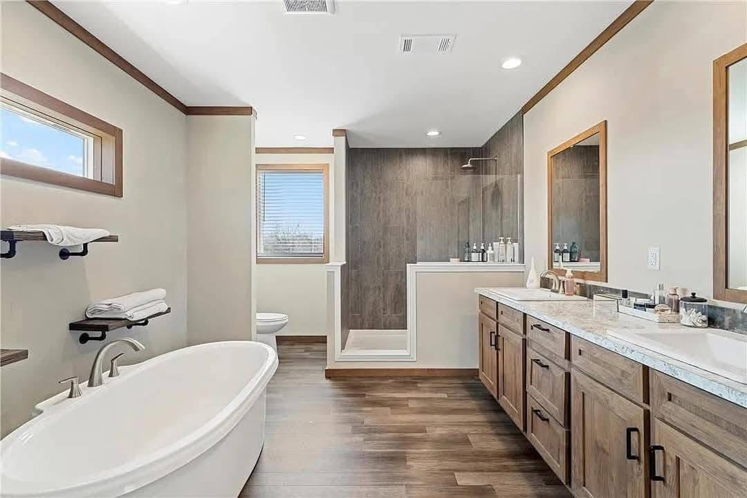 Spacious bathroom with wood accents features a freestanding tub, glass-enclosed shower, double sink vanity, towel shelves, and natural light from a window.