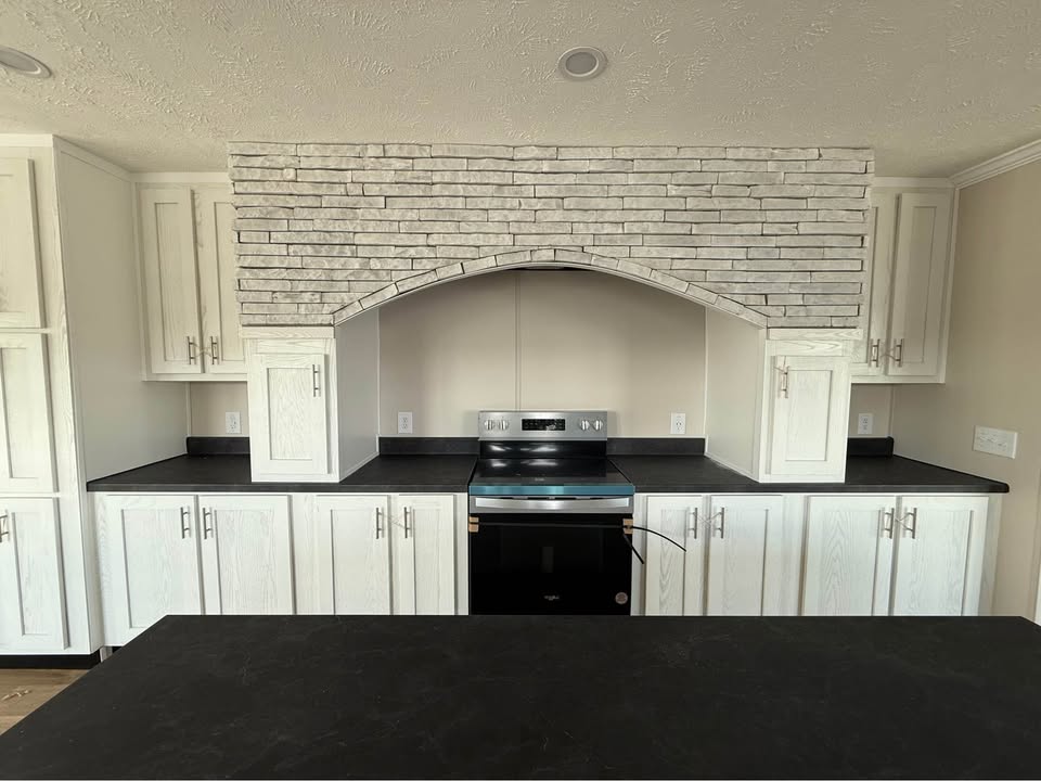 Bright kitchen featuring white cabinets, black countertops, and a modern stainless steel stove. Rustic brick arch accentuates the central cooking area.