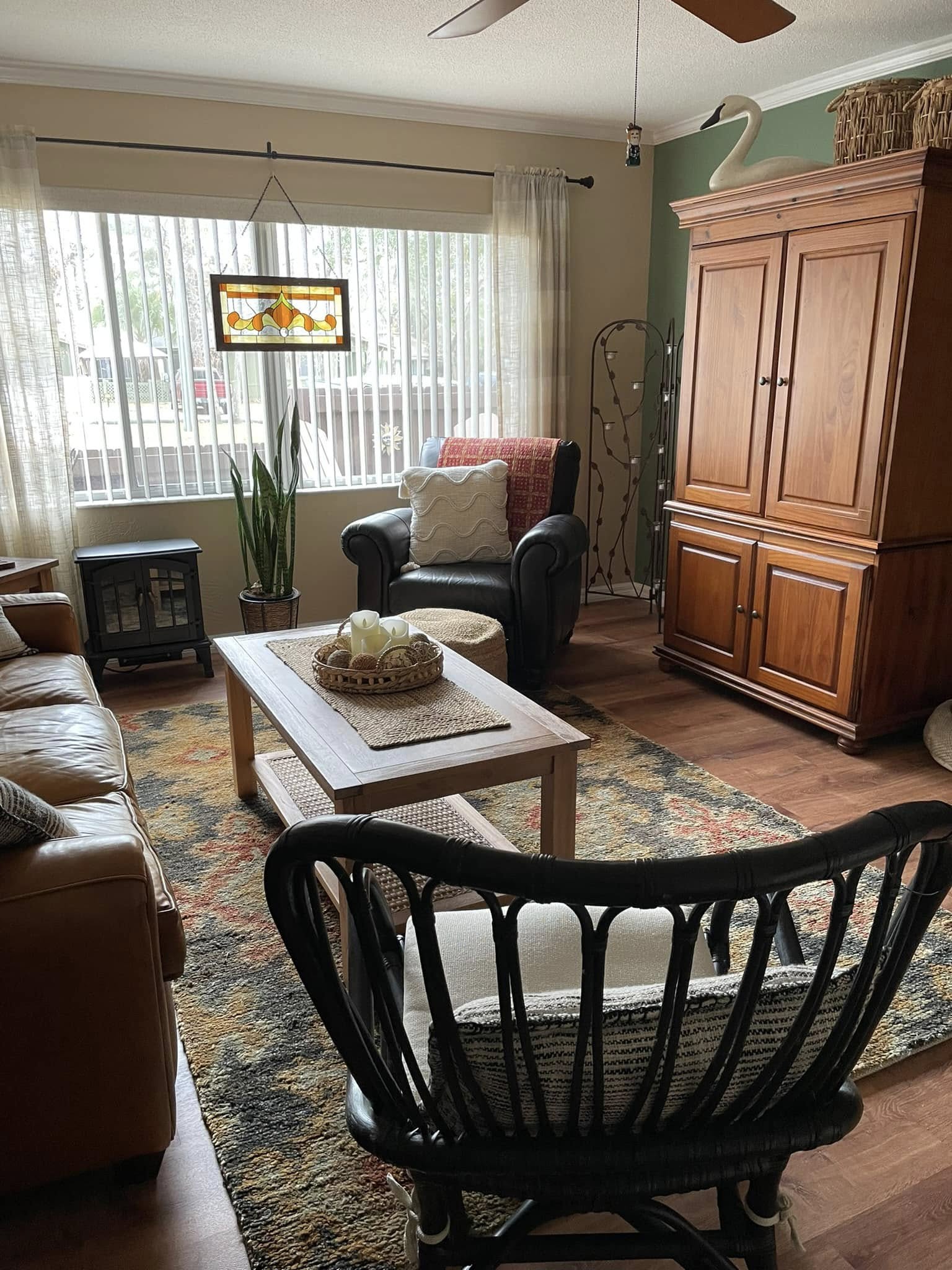 Cozy living room with a leather sofa, armchair, wooden armoire, and a stained glass lamp. Earthy tones and soft lighting create a warm, inviting ambiance.
