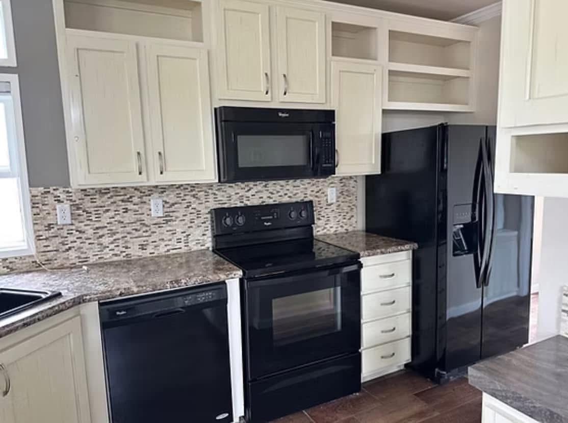 Modern kitchen with cream cabinets, black appliances, mosaic tile backsplash, and dark countertops. Bright and clean atmosphere.