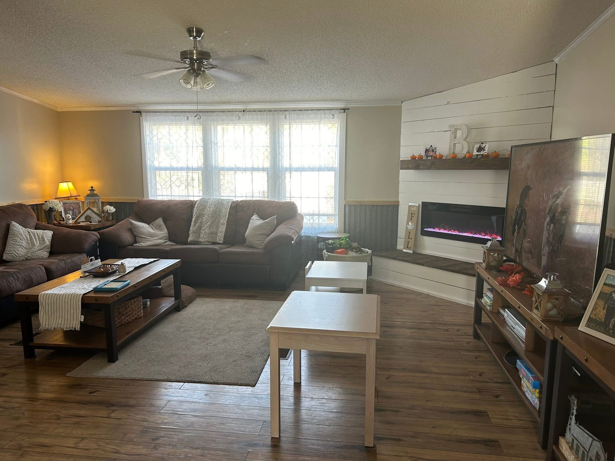 Cozy living room with brown couches, a wooden coffee table, and a lit fireplace. Decor includes autumn accents and soft lighting from lamps.