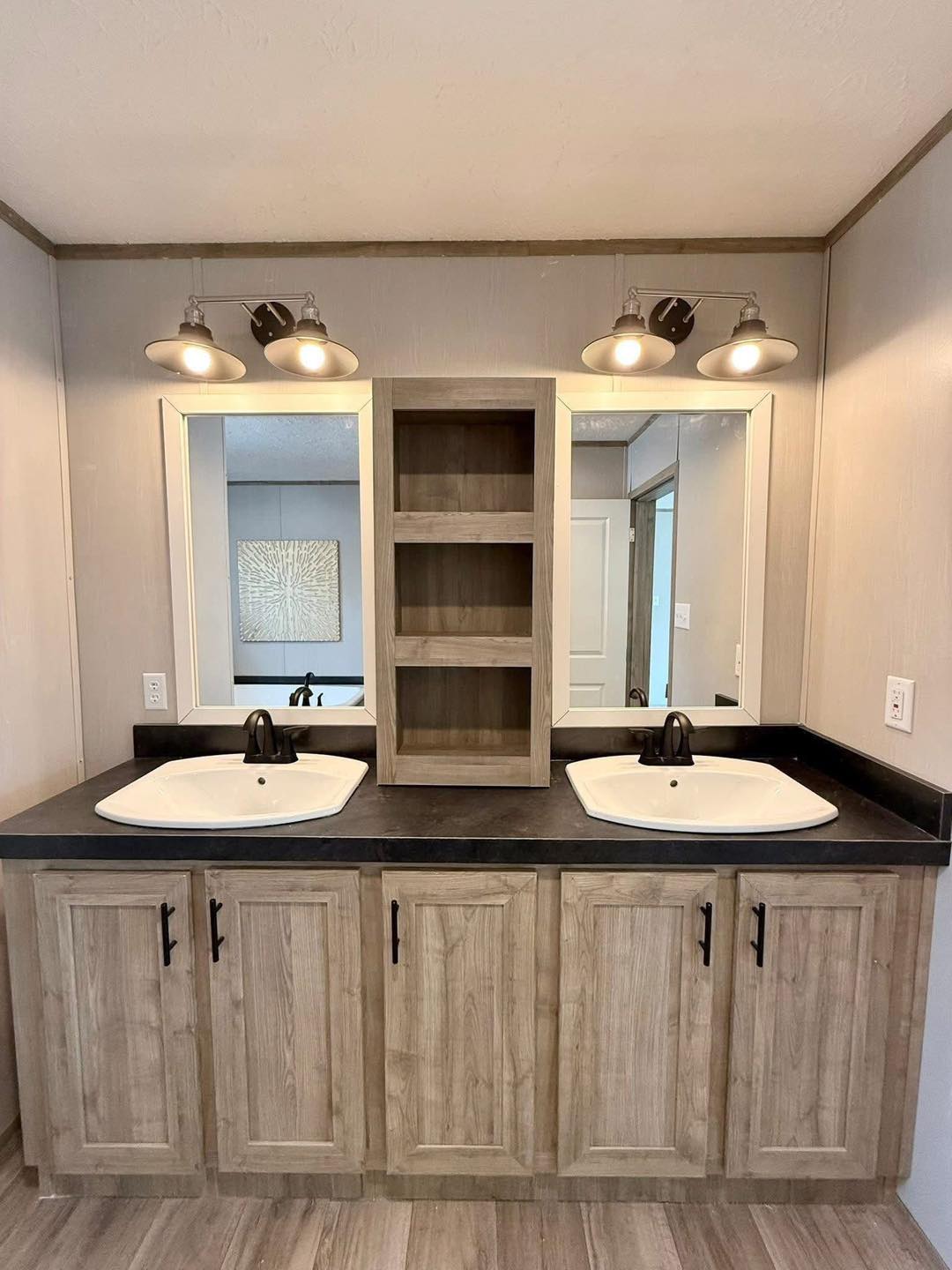 Modern bathroom vanity with dual sinks and matte black faucets. Wooden cabinetry has center open shelves, set between two large mirrors and overhead industrial lights. Neutral tones create a calm ambiance.