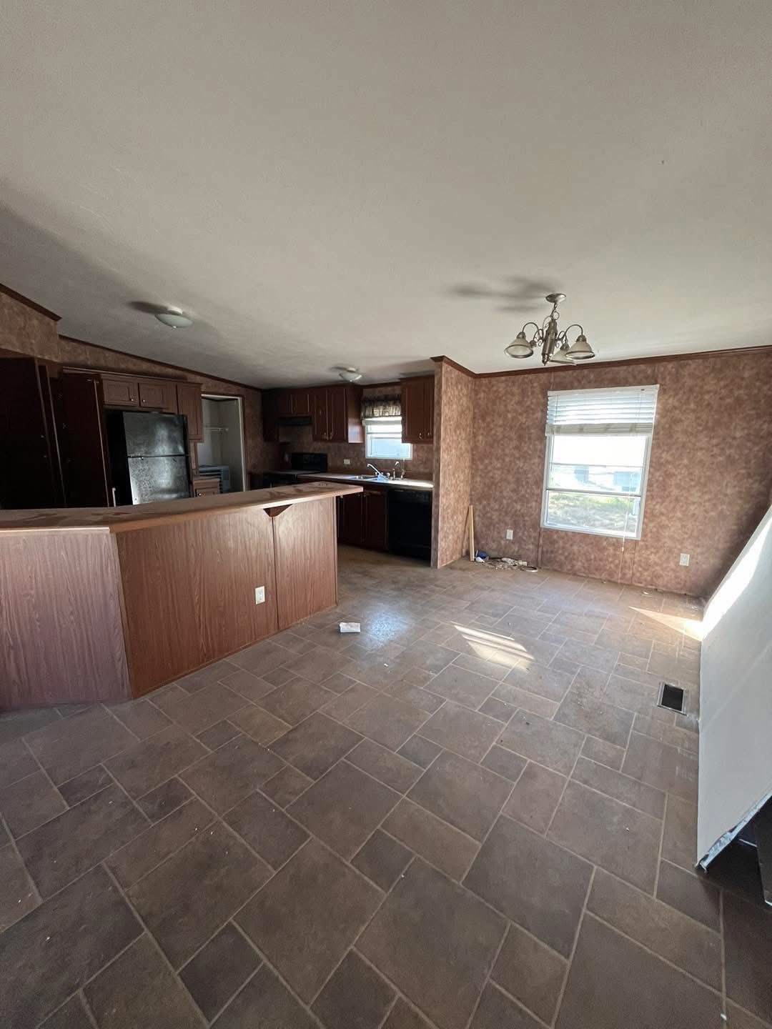 Spacious kitchen with wood cabinets, dark appliances, and a central island under ceiling lights. A window with blinds allows natural light in.