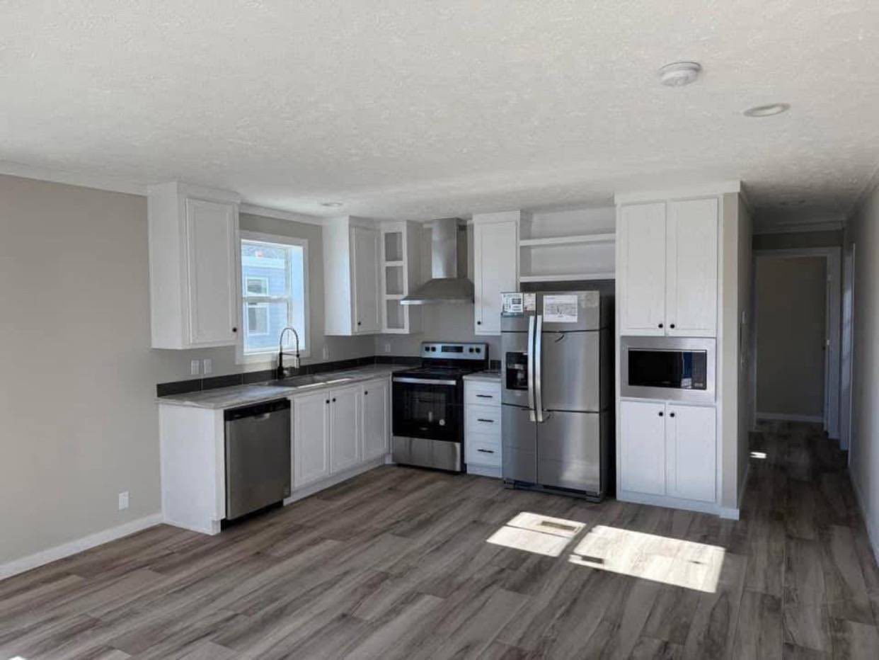 Modern kitchen with white cabinets, stainless steel appliances, and black countertops. Natural light filters through a window, creating a bright, welcoming space.