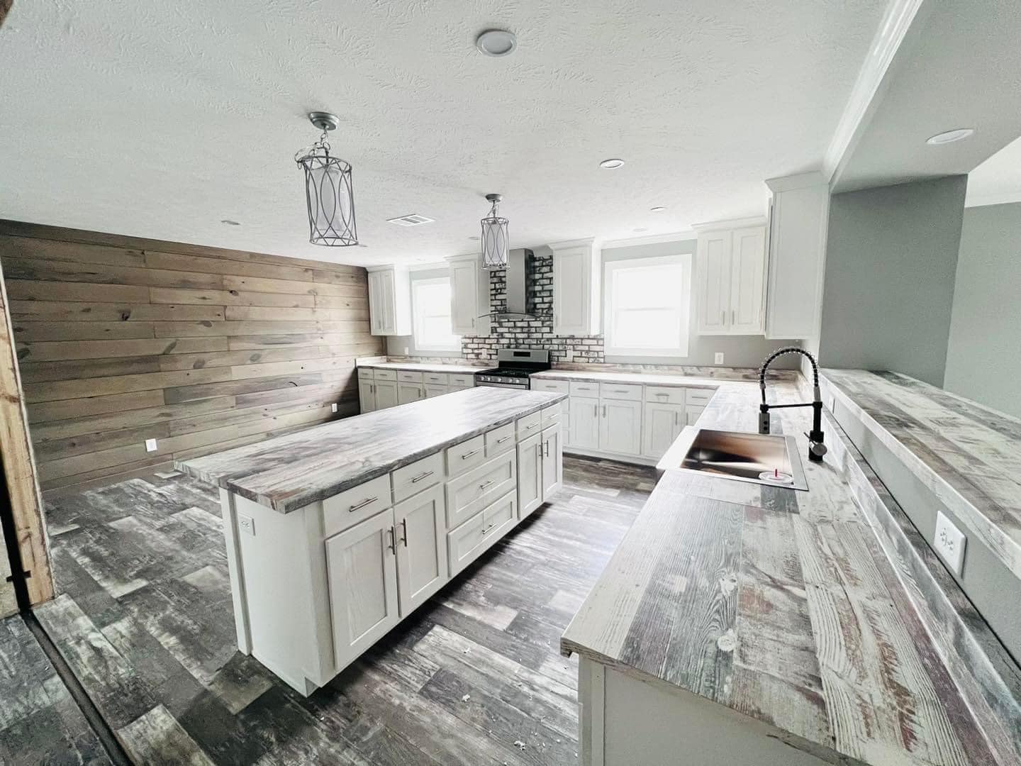 Spacious kitchen with rustic wood paneling, white cabinets, and distressed wood countertops. Brick backsplash and industrial pendant lights create a modern, cozy feel.