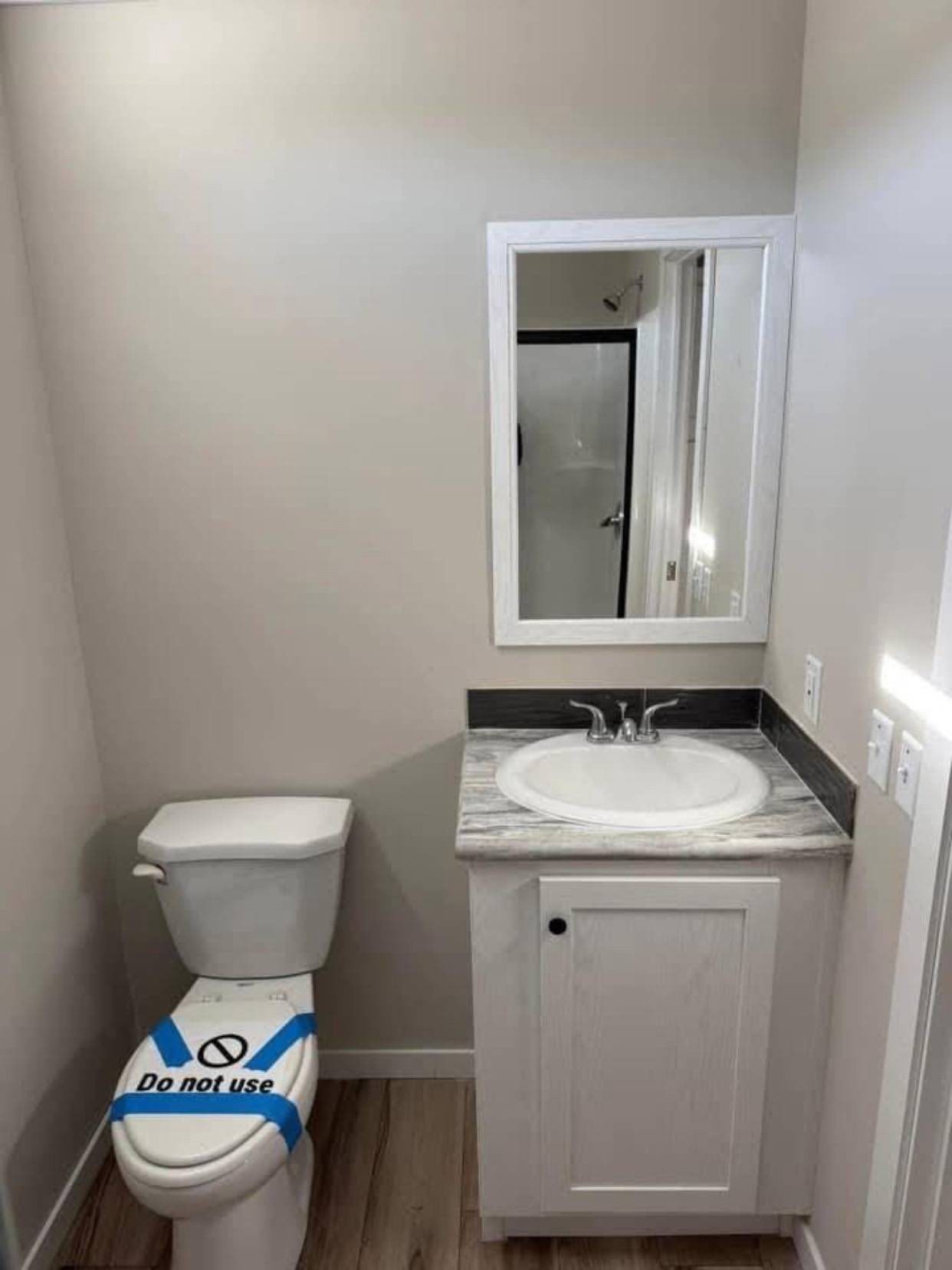 Small bathroom with a white toilet and sink vanity. The toilet is marked with blue tape and a "Do not use" sign. Neutral tones create a minimalistic feel.