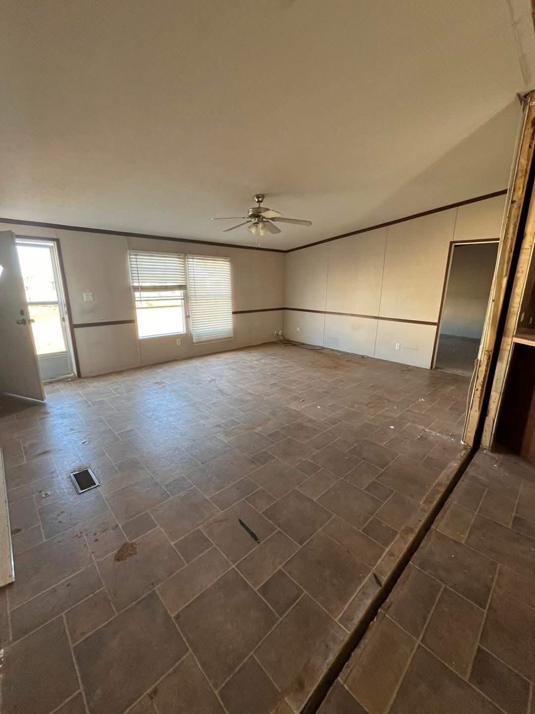 Empty room with tiled floor, beige walls, a ceiling fan, and a door with a window covered by blinds. The space has an unfinished look.