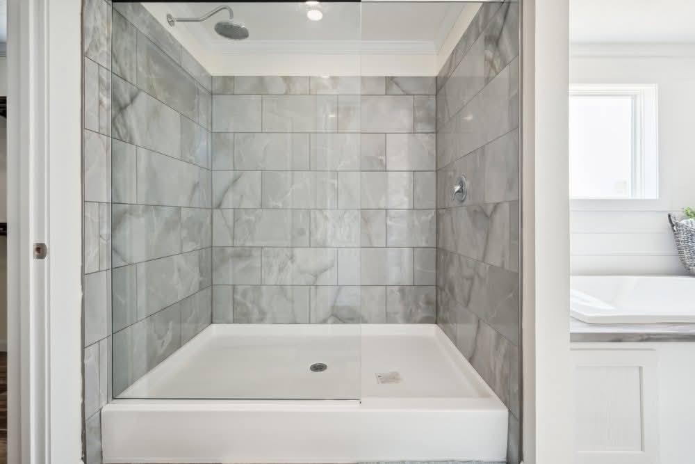 A modern bathroom with a glass-enclosed shower featuring gray marble tiles, a rain shower head, and a bright, calming ambiance.