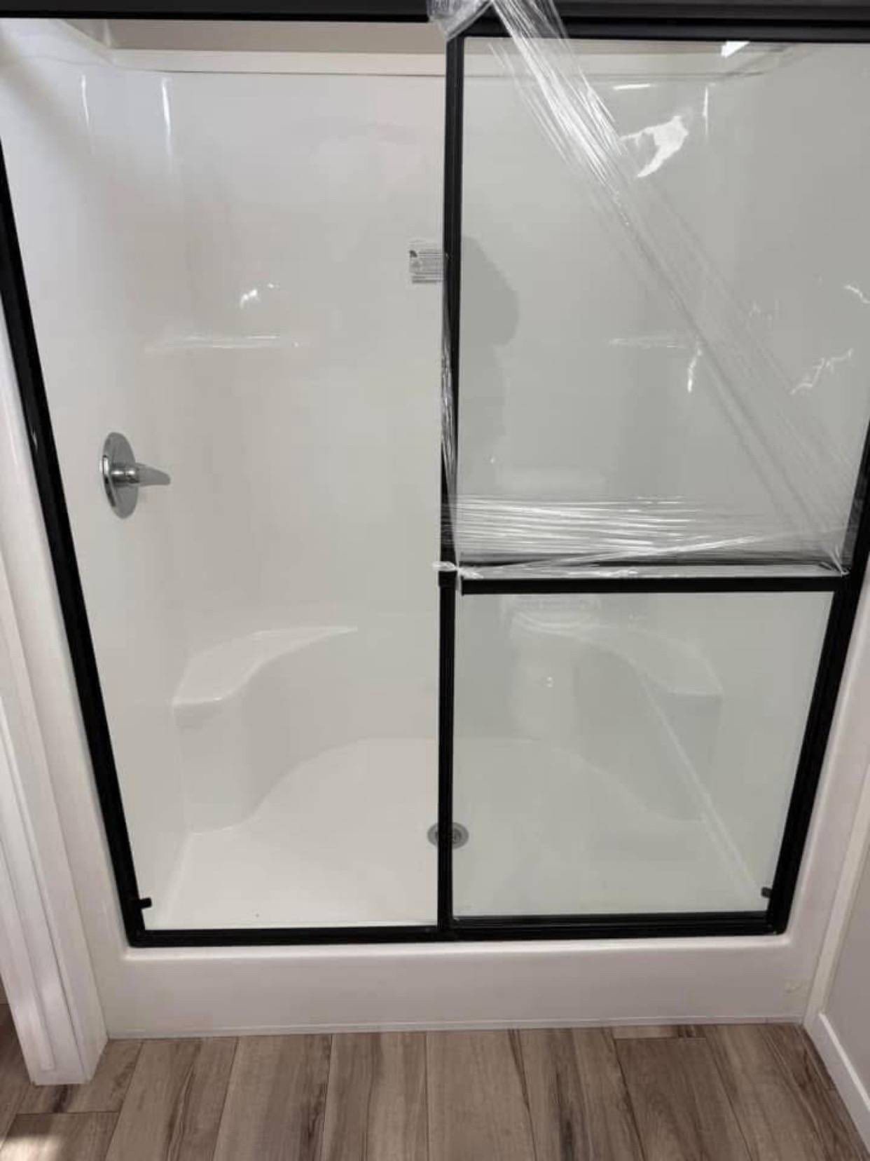 Modern shower with clear glass doors framed in black and a built-in seat. The wooden floor adds a warm contrast to the sleek design.